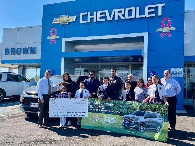 Winners pose with prize cheque and banner in front of Chevrolet showroom